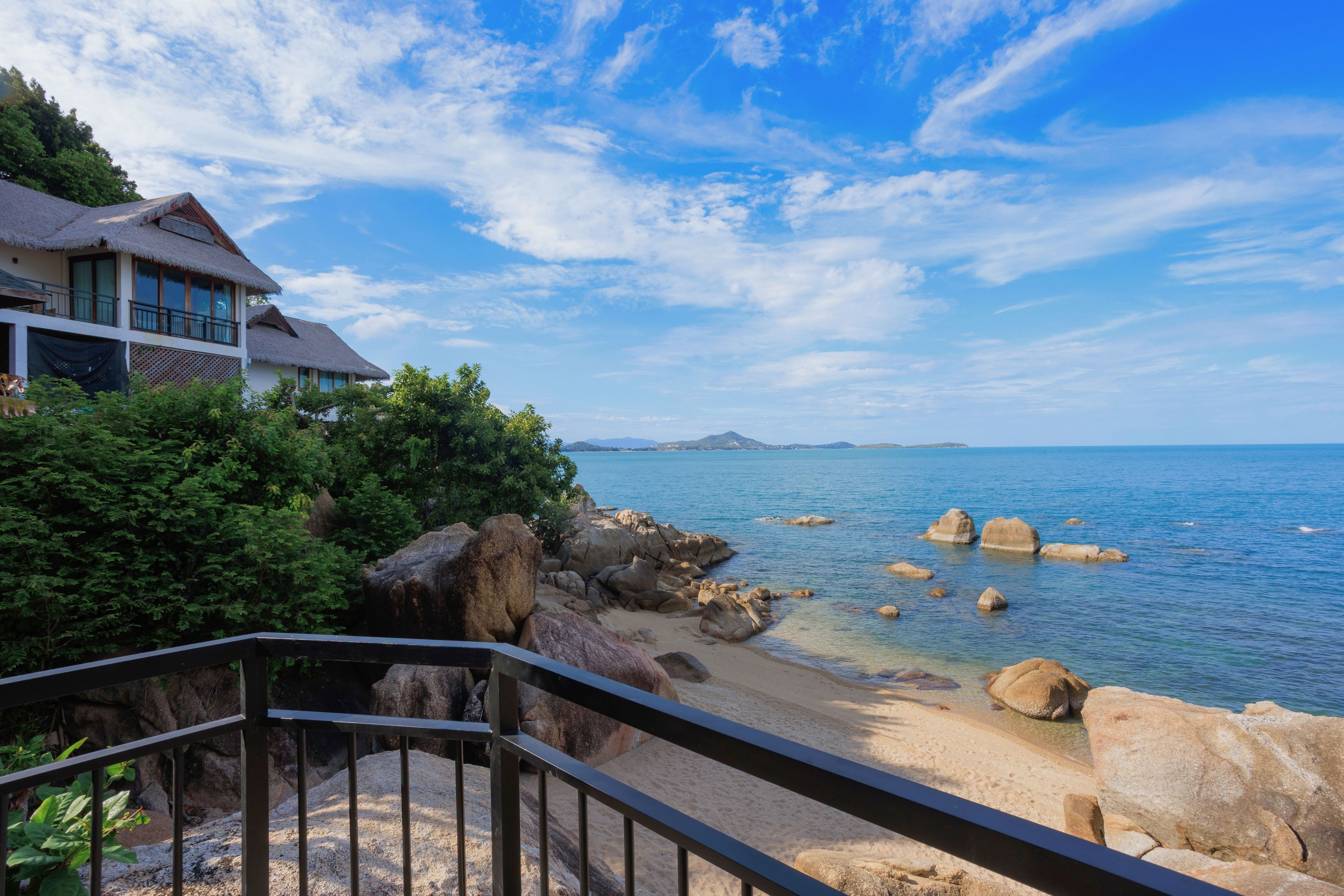 A coastal property with a thatched-roof building, a rocky shoreline, and a clear view of the sea.