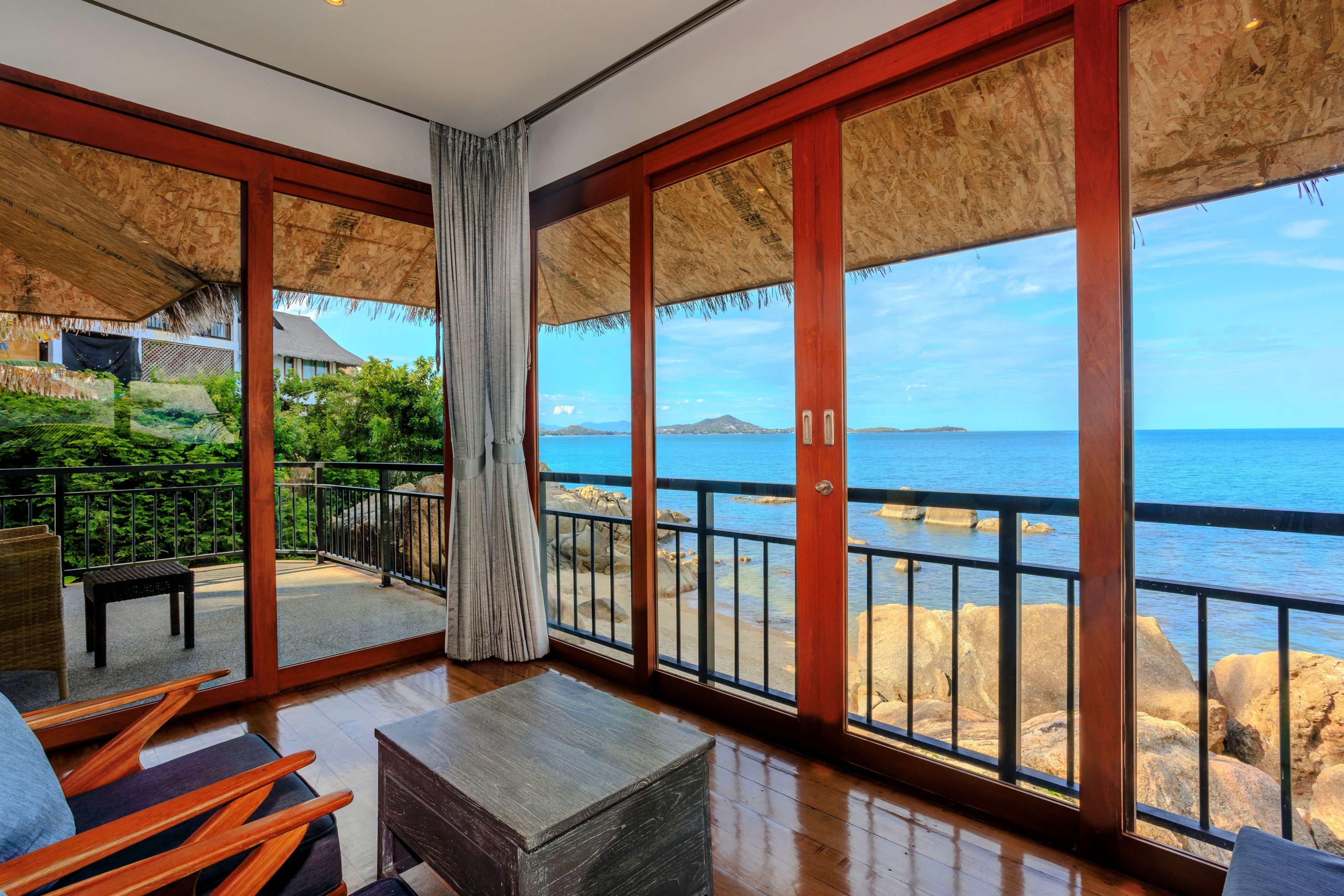 A room with a large glass door leading to a balcony overlooking a rocky coastline.