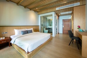 A modern bedroom with a large bed, wooden headboard, a desk with a chair, and a glass-enclosed shower area.