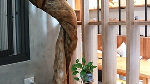 Ein Zimmer mit einer einzigartigen Holzskulptur, einer kleinen Pflanze auf einem Holzschemel und Blick auf eine Holzkonstruktion im Freien.