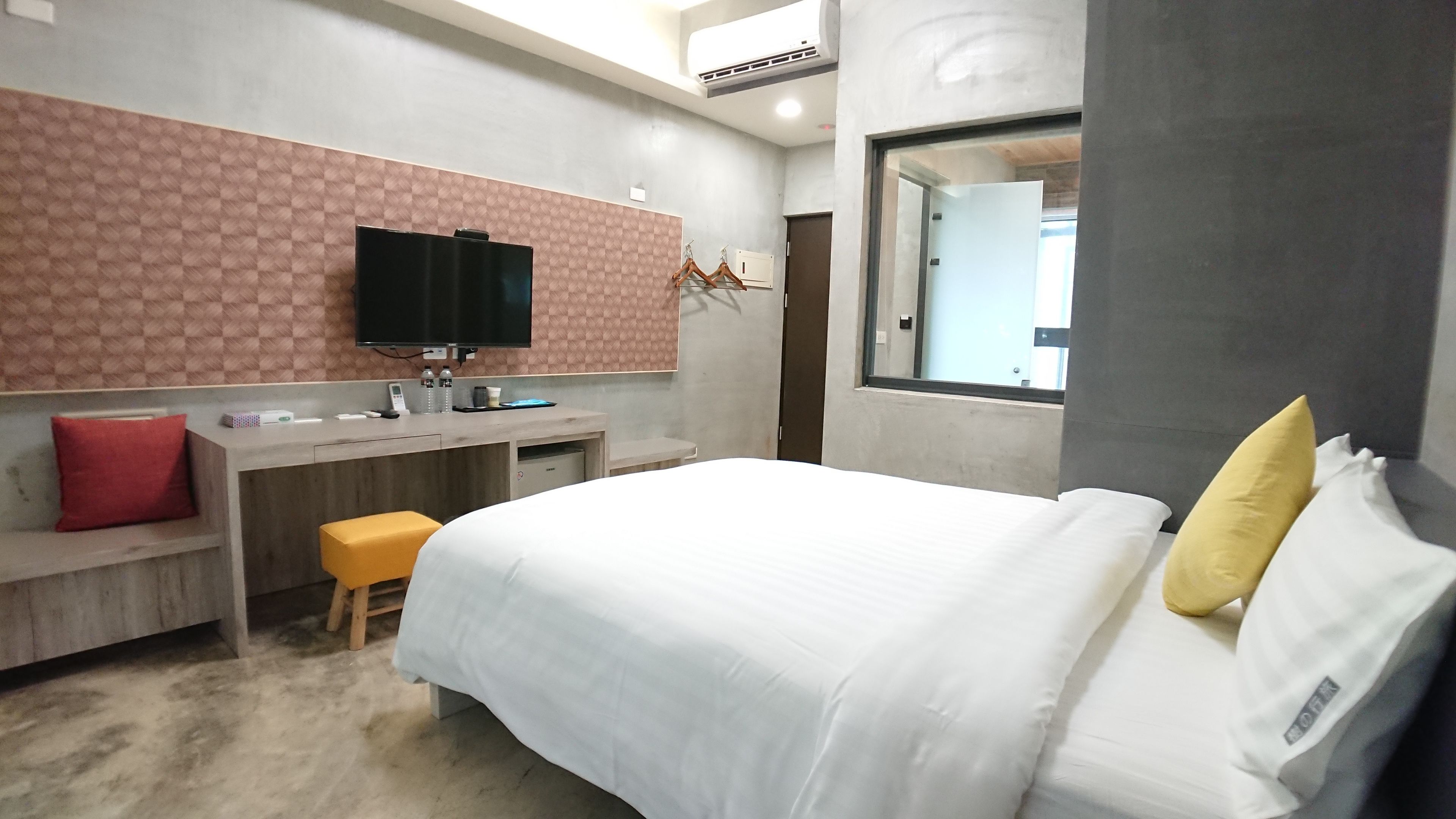 A modern hotel room with a bed, a desk, a television, and a mirror.