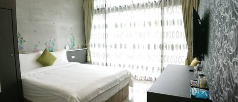 A bedroom with a bed, a desk, a laptop, and a television.