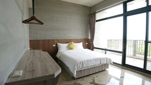 A modern hotel room with a wooden headboard, a large window with a view of the outdoors, a wooden nightstand, and a bed with white bedding and a yellow pillow.