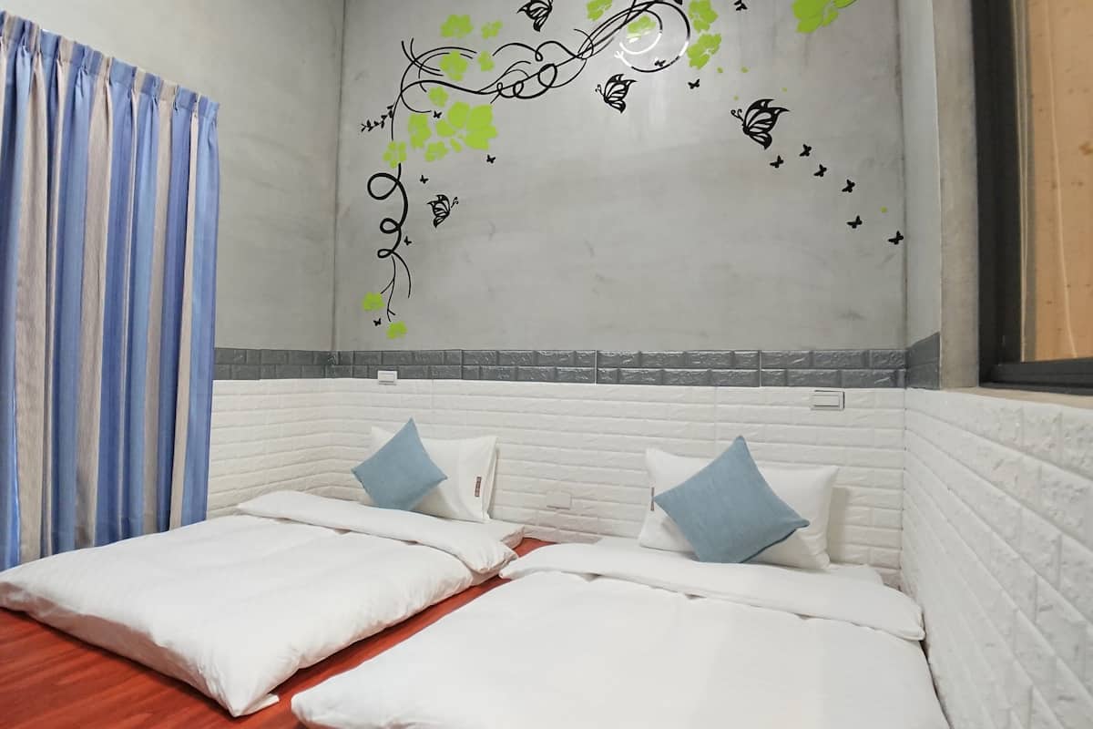 A bedroom with a bed, two pillows, a window with curtains, and a wall with decorative stickers.