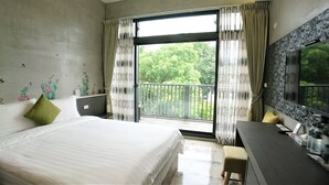 Ein Hotelzimmer mit Bett, Schreibtisch, Stuhl, einem großen Fenster mit Vorhängen und einem Balkon mit Geländer.