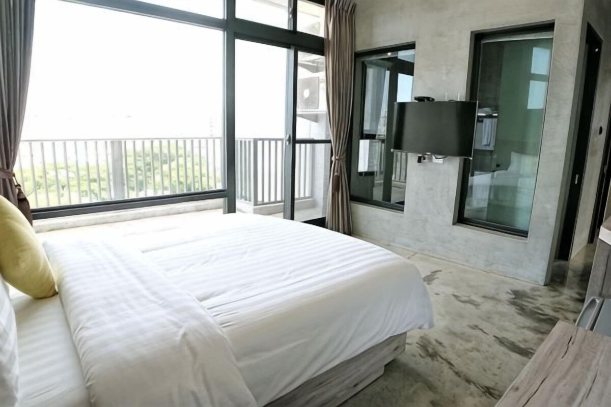 A hotel room with a large bed, a TV mounted on the wall, and a balcony with a view.