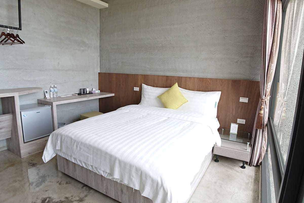 A modern hotel room with a bed, bedside tables, a desk, and a wardrobe.