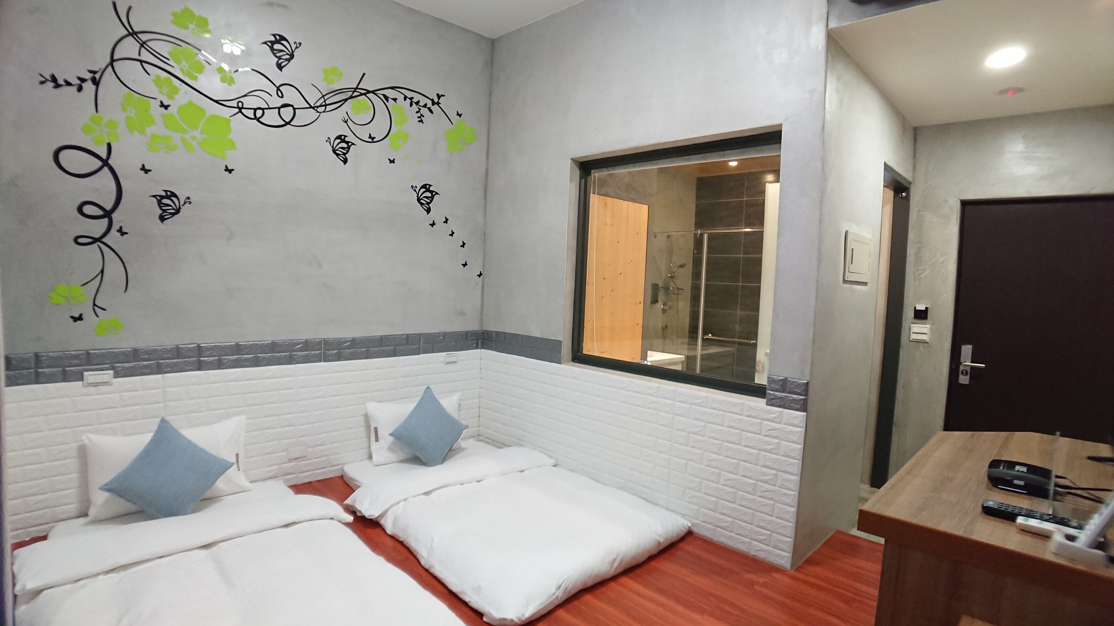 A hotel room with two beds, a window, a mirror, and a wooden desk with a remote control.