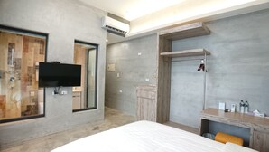 Ein modernes Hotelzimmer mit einem großen Bett, einem an der Wand befestigten Fernseher, einer Duschkabine und einem Holzinlay mit einem Spiegel.