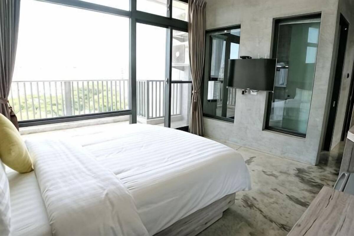 A hotel room with a large bed, a TV mounted on the wall, and a balcony with a view.