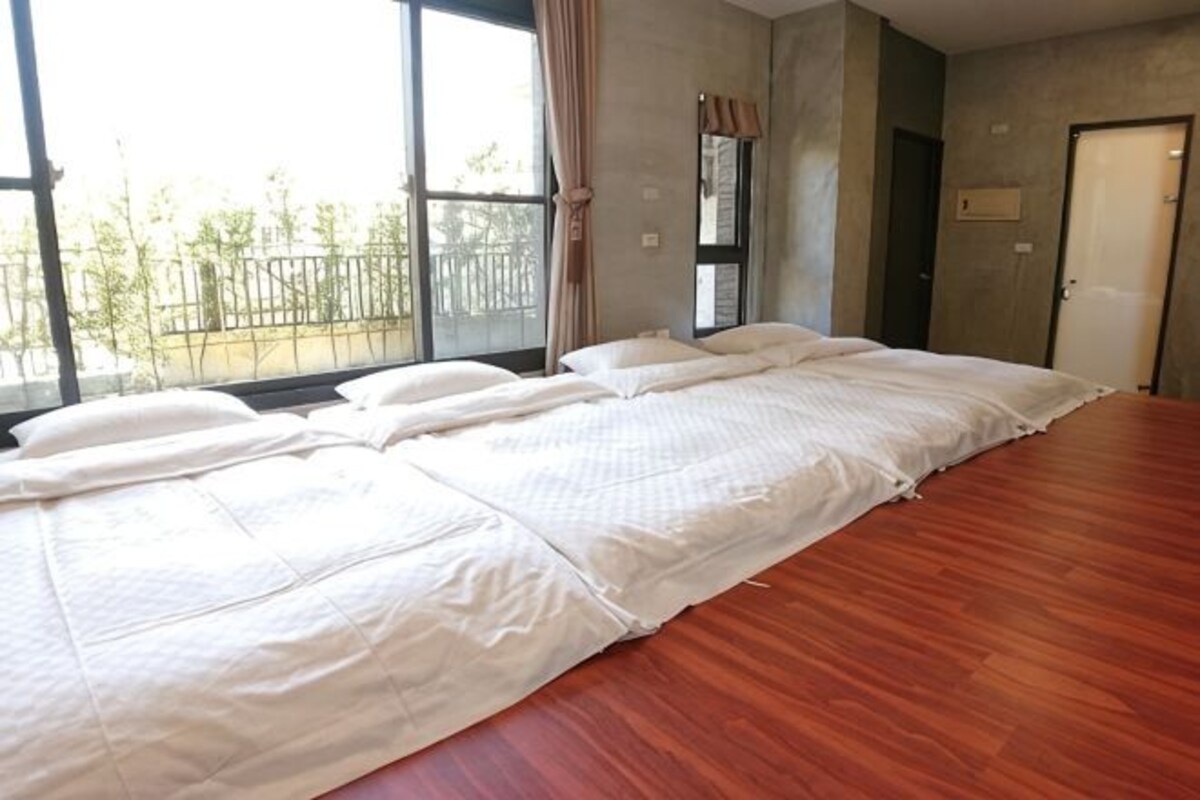 A hotel room with a large bed, a window with curtains, and a view of trees outside.