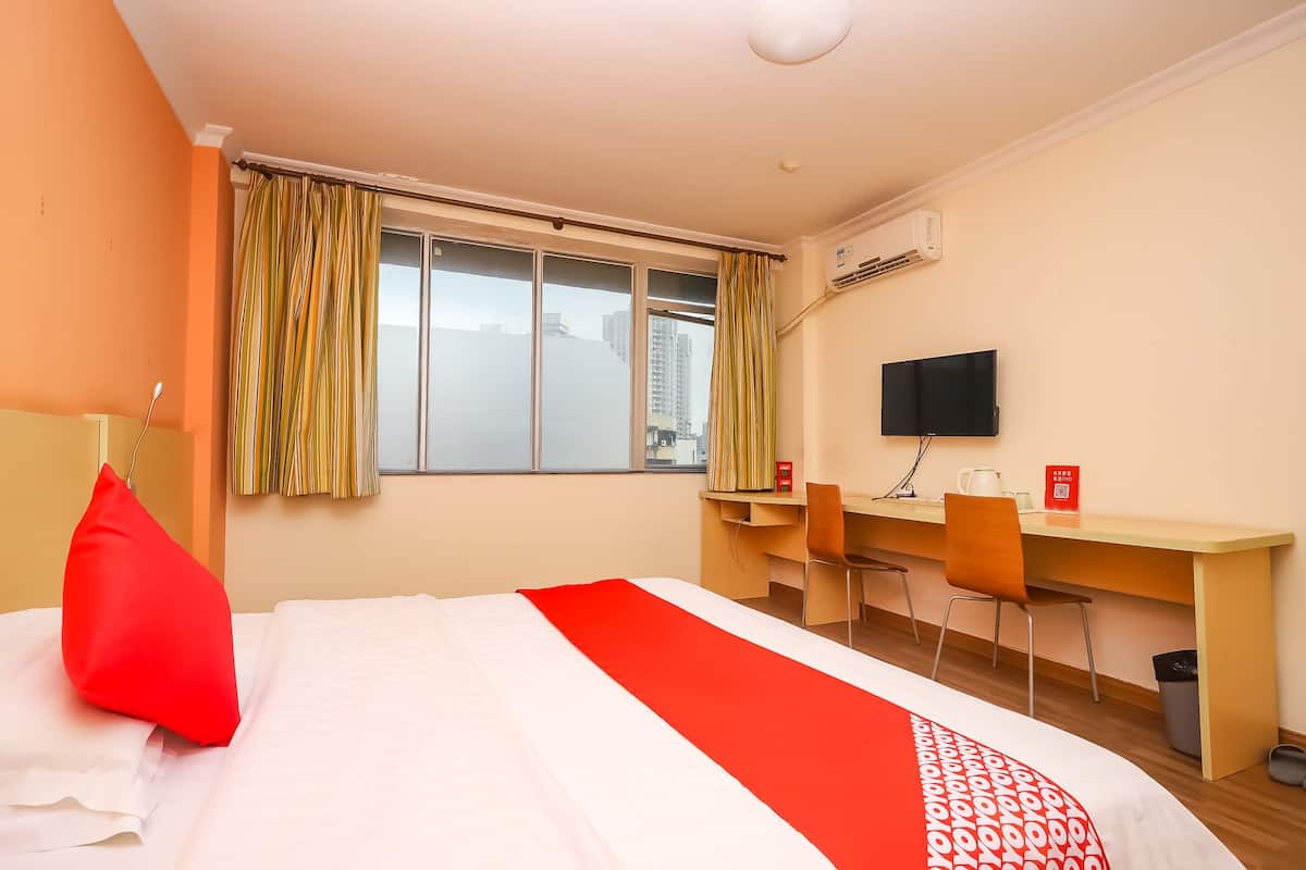 A hotel room with a bed, a desk, two chairs, a TV, and a window with curtains.