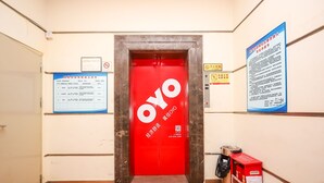 An elevator with a red door and the logo "OYO" on it, a blue informational board to the left, and a red vending machine to the right. - YuanMan Hotel (Huizhou)