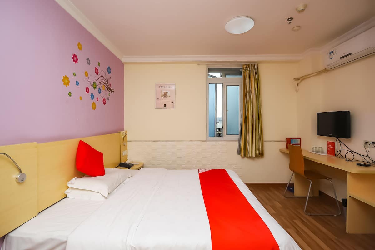 A hotel room with a bed, a desk, a TV, and a window with curtains.