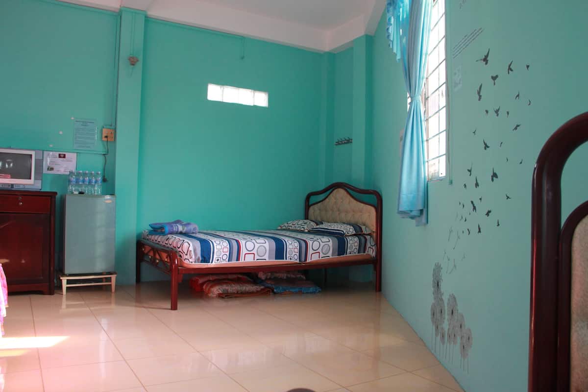 Een kamer met blauwgroene wanden, een bed met beddengoed met een patroon, een kleine televisie op een houten kast en een raam met gordijnen.