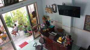 A room with a desk, chair, and a television on the wall. There are potted plants and a window with a view of greenery outside.
