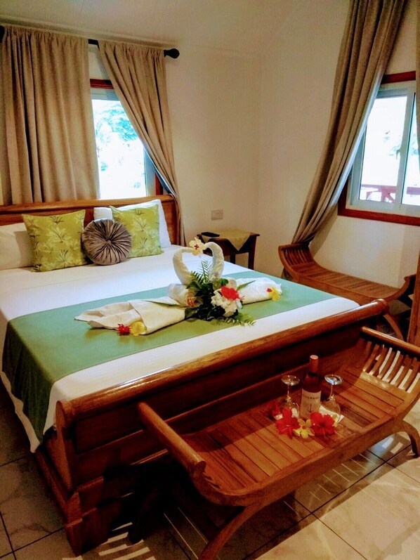 A hotel room with a bed, a wooden bench, and a small table with bottles. - Lucy's guesthouse (La Digue)