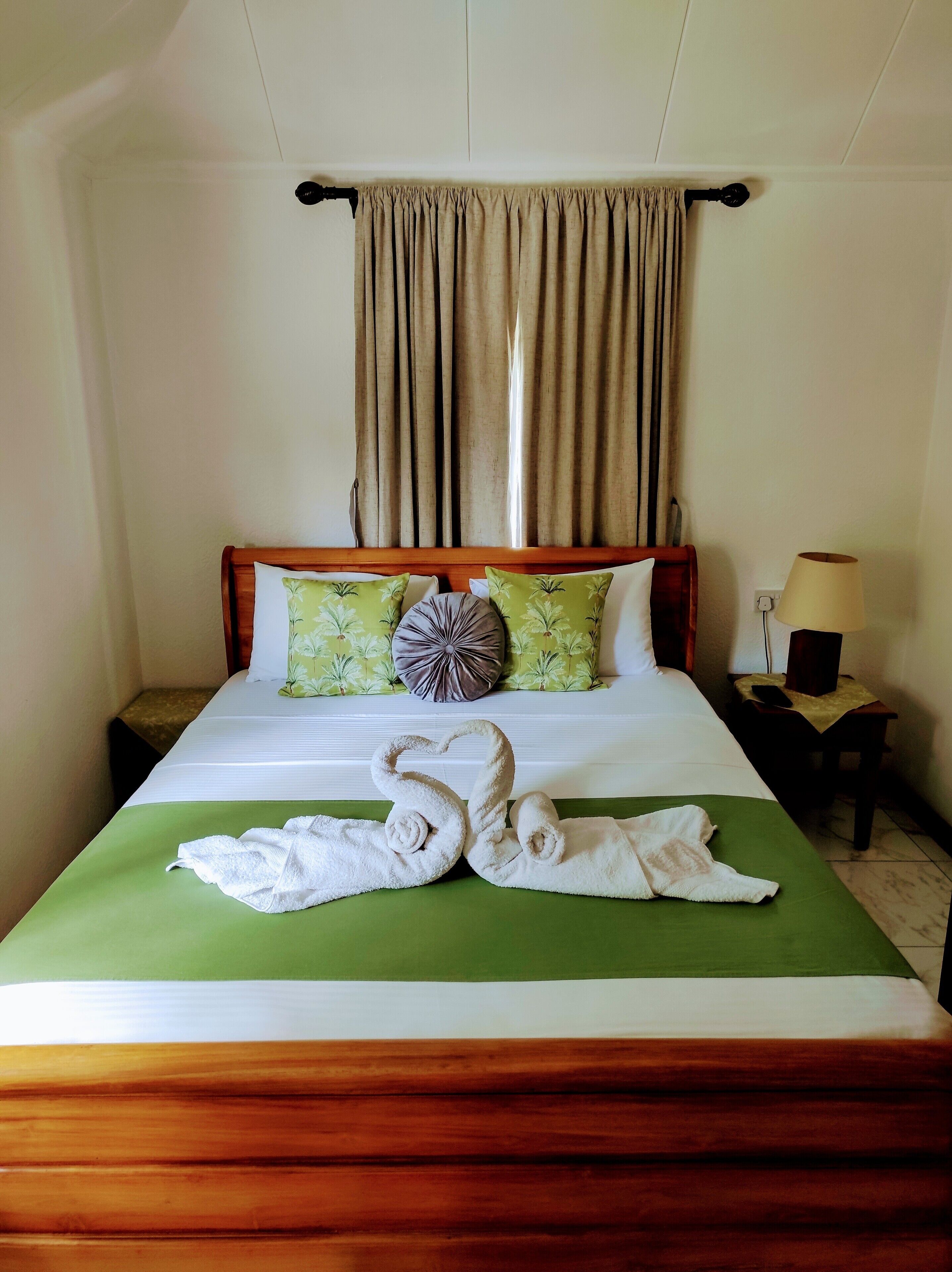 A neatly made bed with a green bedspread and two towels arranged in a swan shape.