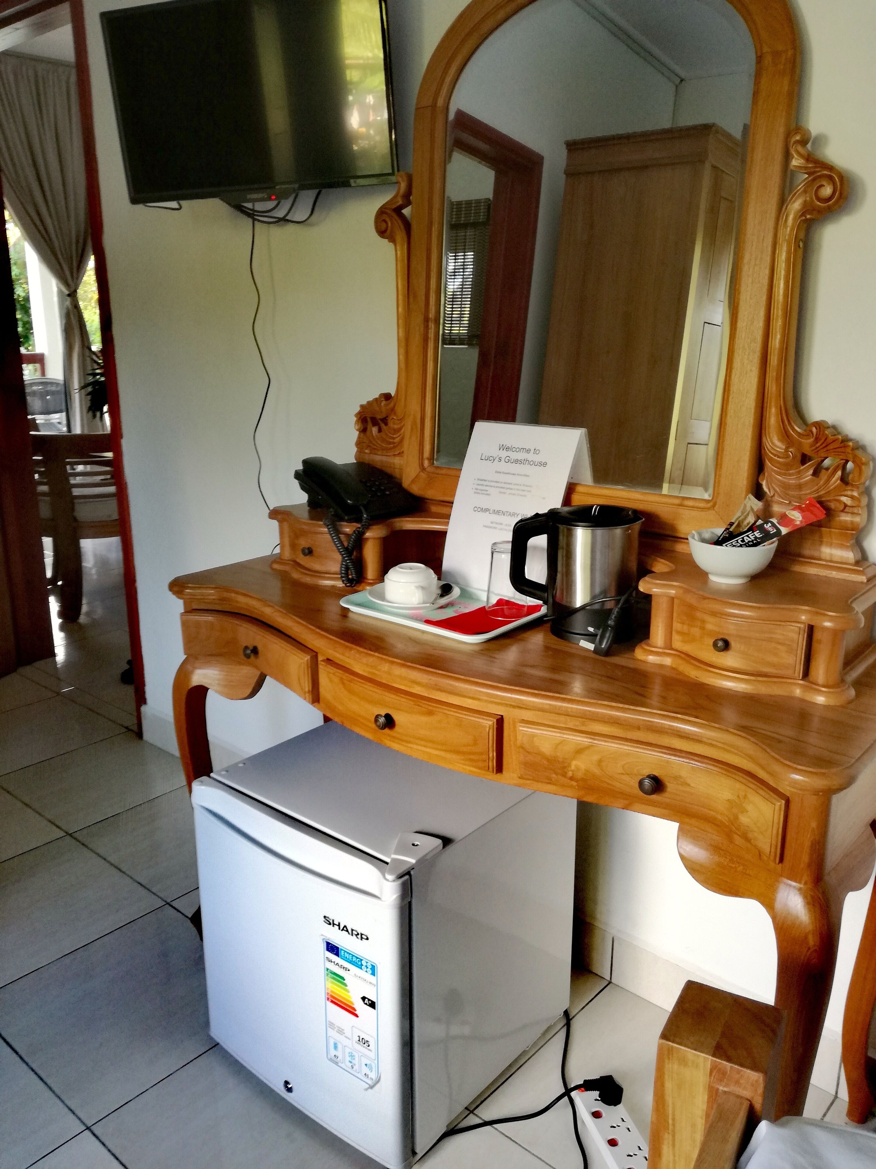Uma mesa de madeira com um espelho, uma cafeteira, uma tigela, uma chávena e um aviso dando as boas-vindas aos hóspedes.