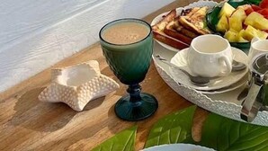 A breakfast setting with a plate of crepes, a cup of coffee, and a fruit platter on a wooden table. - Lucy's guesthouse (La Digue)