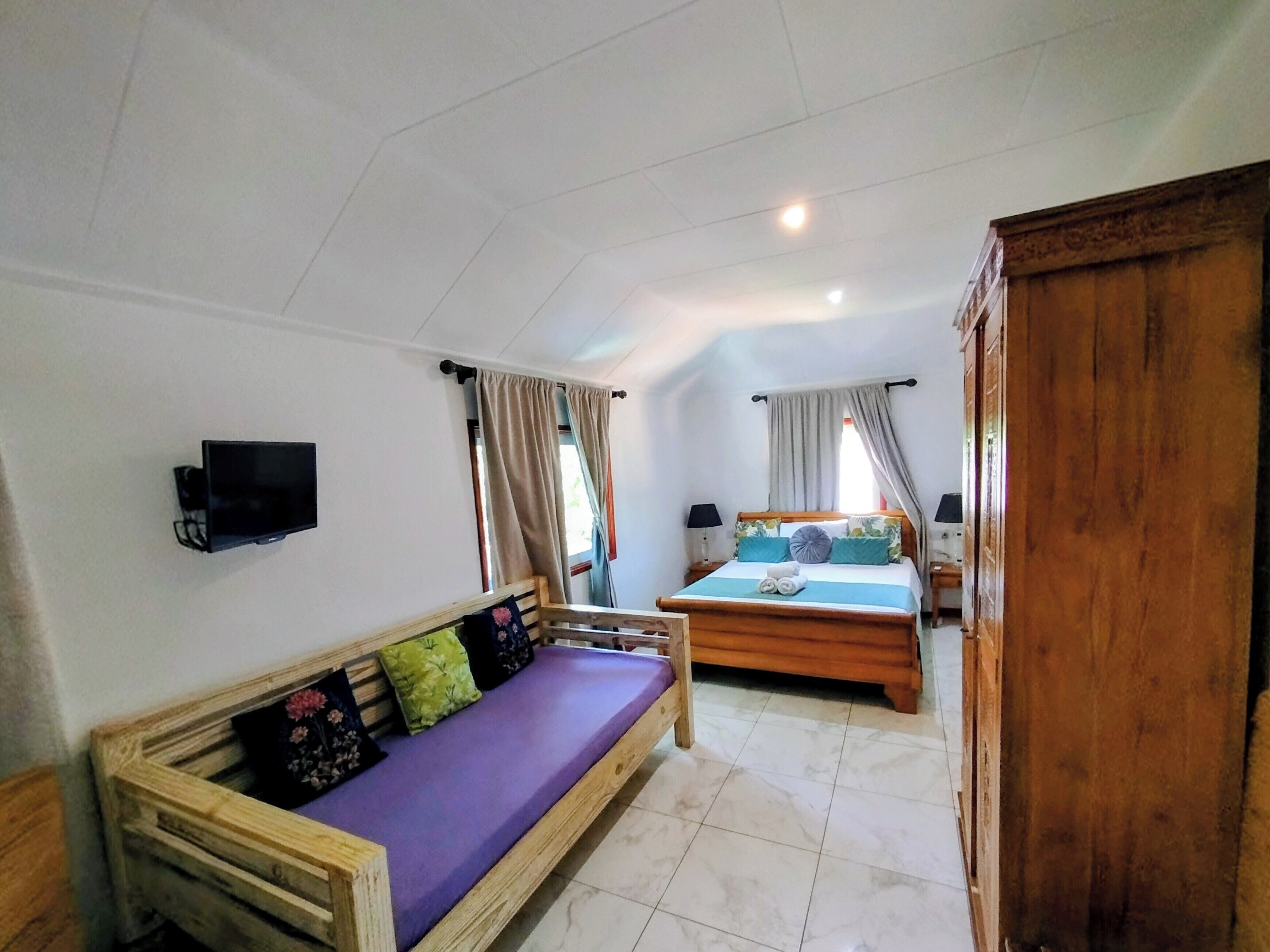 A bedroom with a bed, a wooden bench, a television, and a wardrobe.