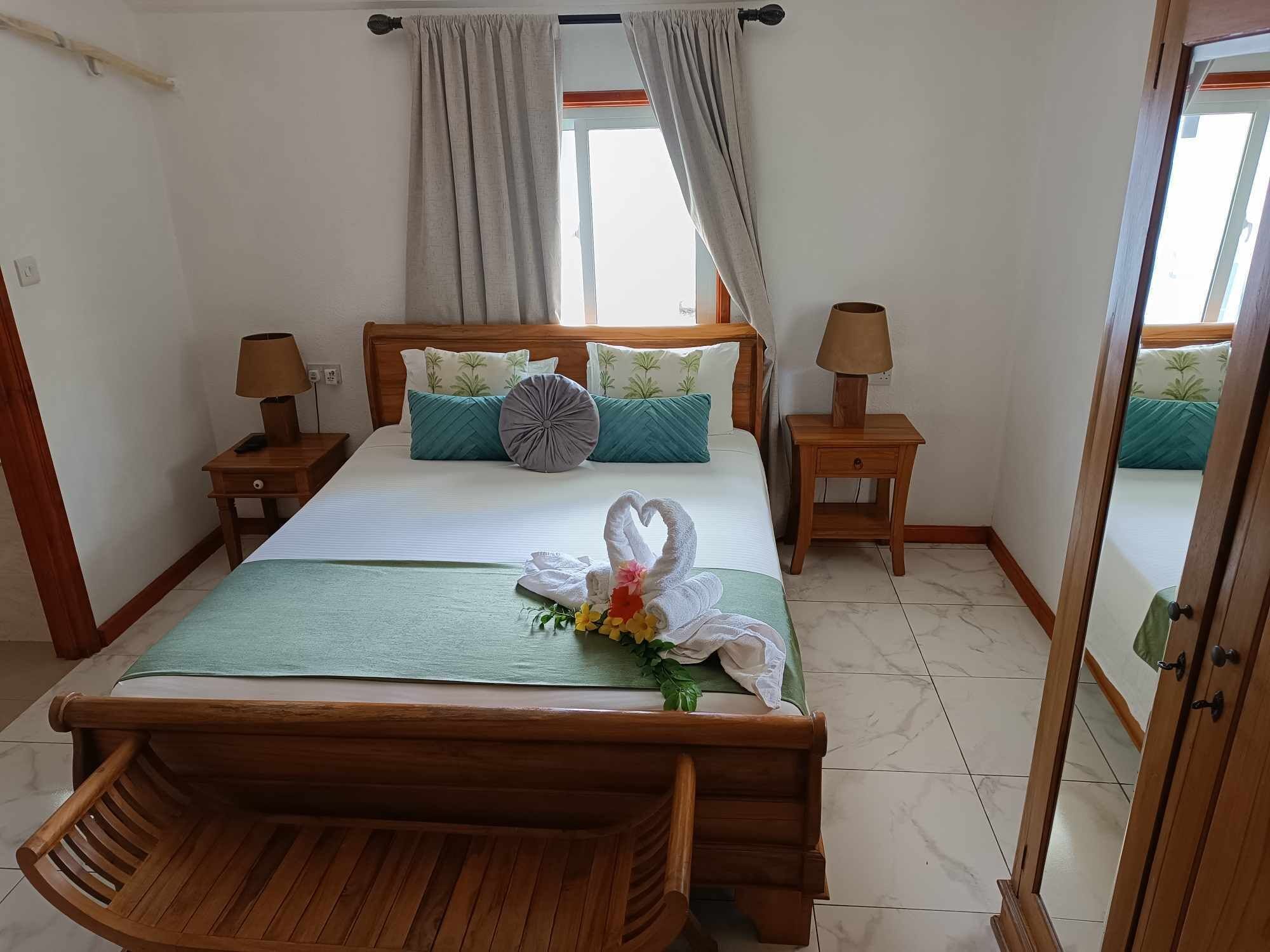 A neatly arranged hotel room with a wooden bed, two bedside tables with lamps, a wooden bench, and a mirror.