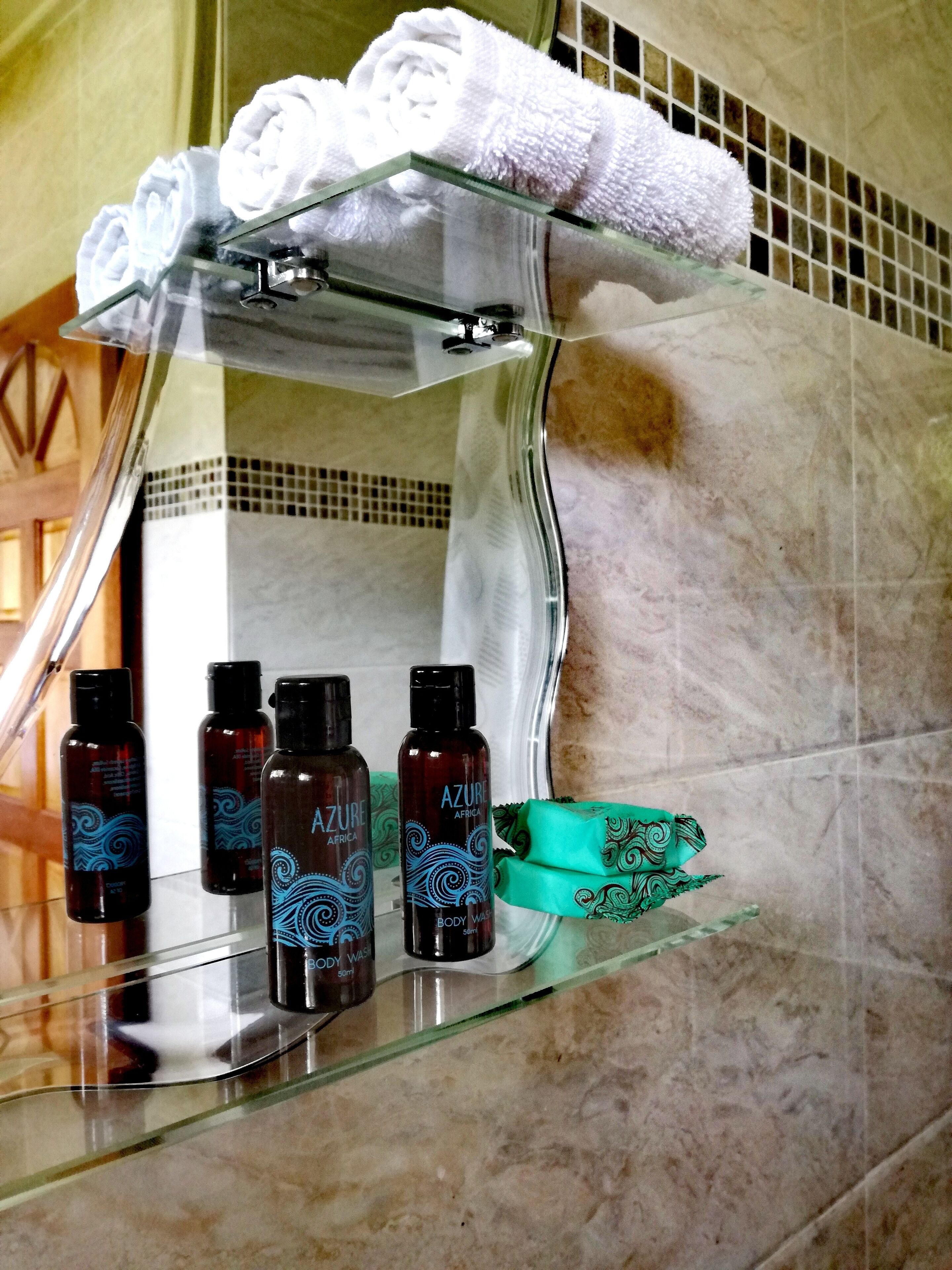 A bathroom with a glass shelf holding toiletries and a towel rack above it.
