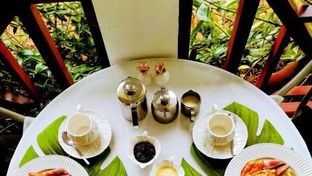 A round table with a variety of breakfast items including toast, omelets, and fruit, surrounded by cups and condiments. - Lucy's guesthouse (La Digue)