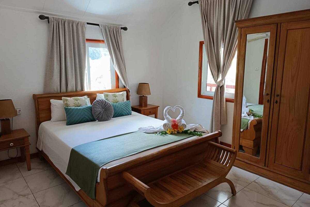 A neatly arranged bedroom with a wooden bed, a bench, a nightstand with a lamp, and a wardrobe.
