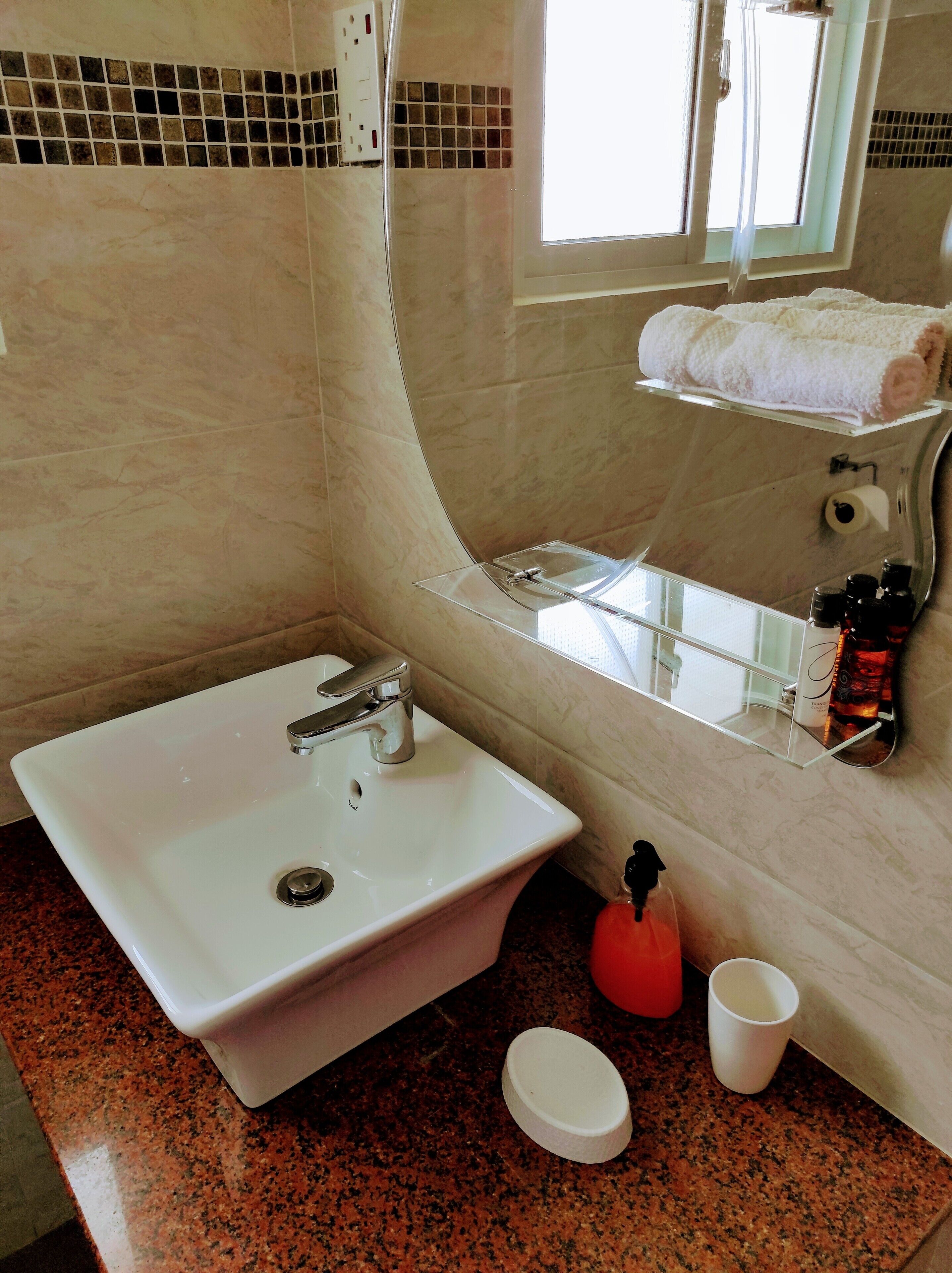 A bathroom with a white sink, a glass shower enclosure, a towel rack, and a bottle of soap.