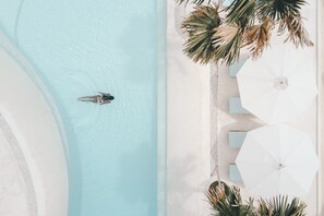 An aerial view of a swimming pool with a person in the water, surrounded by palm trees and white umbrellas. - Canggu Village (Canggu)
