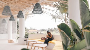 Un espacio exterior moderno con una decoración en blanco y amarillo, que incluye una persona sentada en un banco, una mesa y luces colgantes.