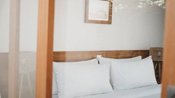 Una cama bien hecha con sábanas blancas, cabecera de madera y un cuadro en la pared.