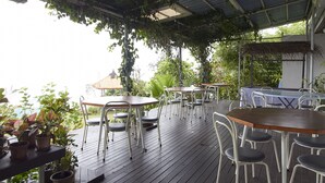 An outdoor patio with wooden tables and chairs, surrounded by potted plants and a metal roof. - Bellevue The Penang Hill Hotel, Bukit Bendera (George Town)