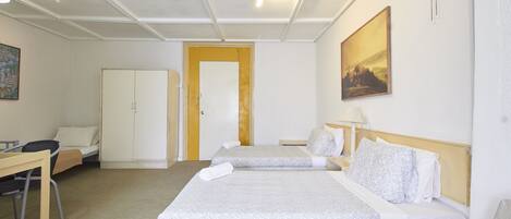 Habitación de hotel con dos camas, un escritorio, una silla, un armario y un ventilador de techo.