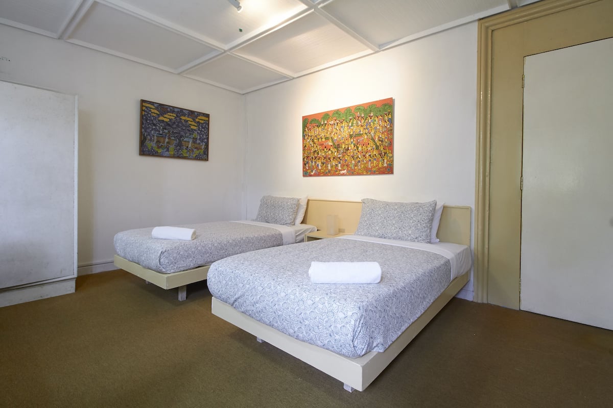 A hotel room with two beds, a painting on the wall, and a door.