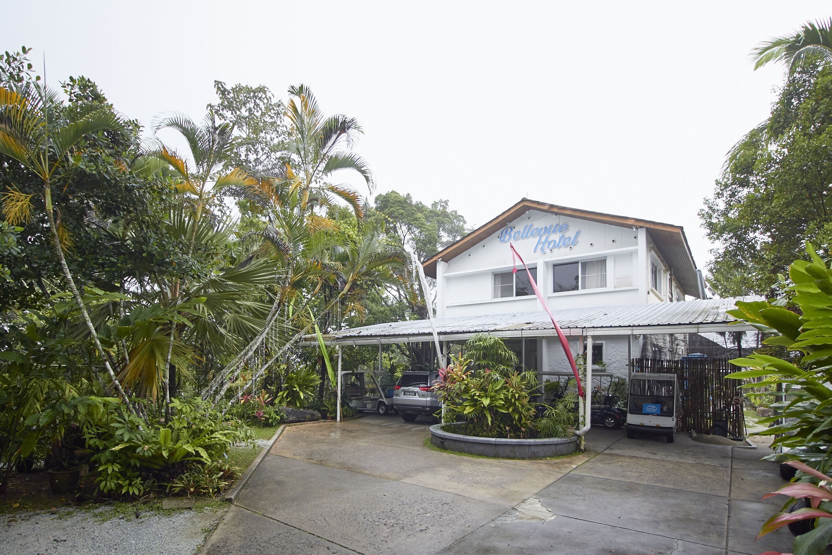A white building with a sign reading "Bellevue Hotel." It has a covered outdoor area with a car and a small truck parked.