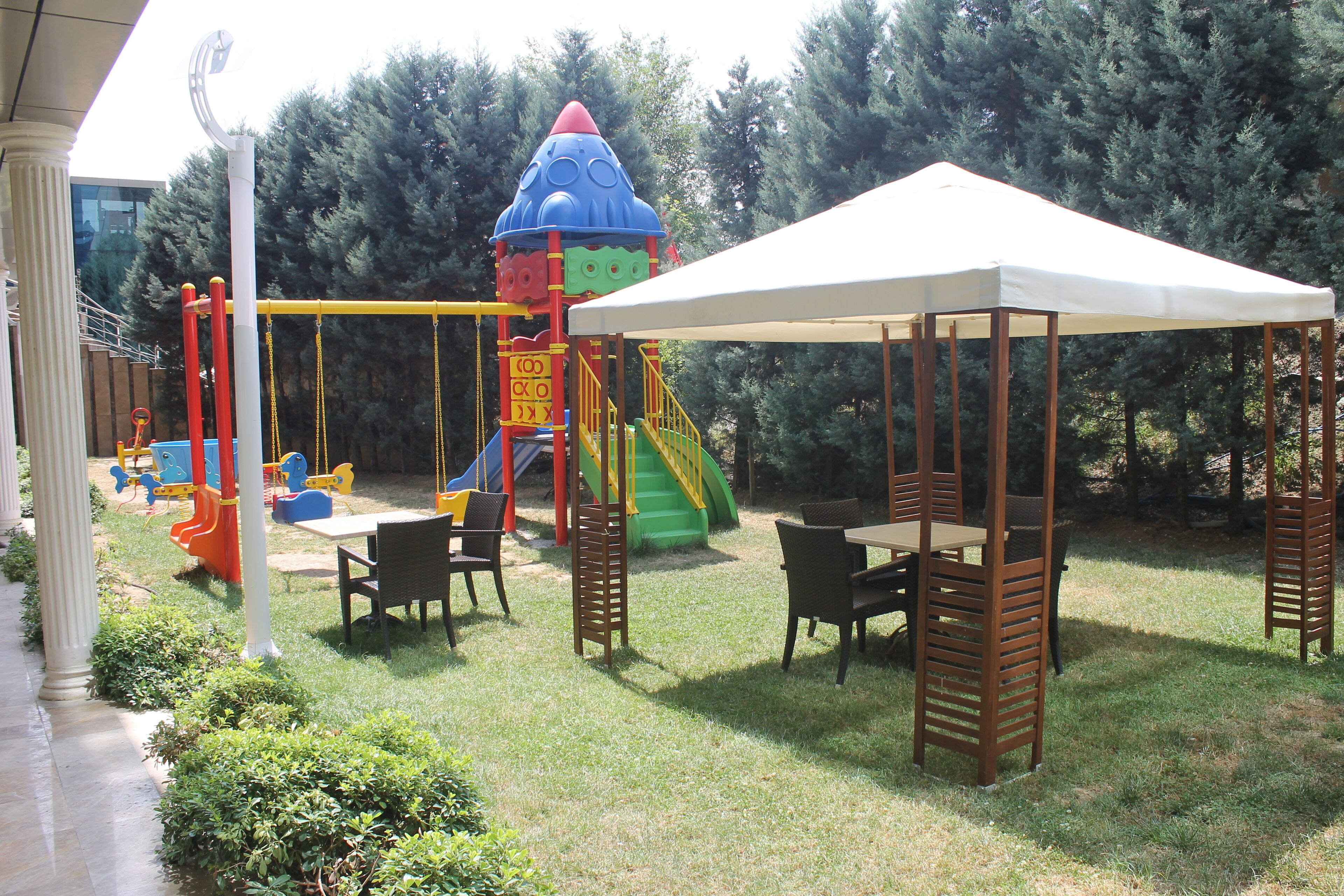 Un parque infantil con columpios y toboganes, un área de picnic techada y un césped.