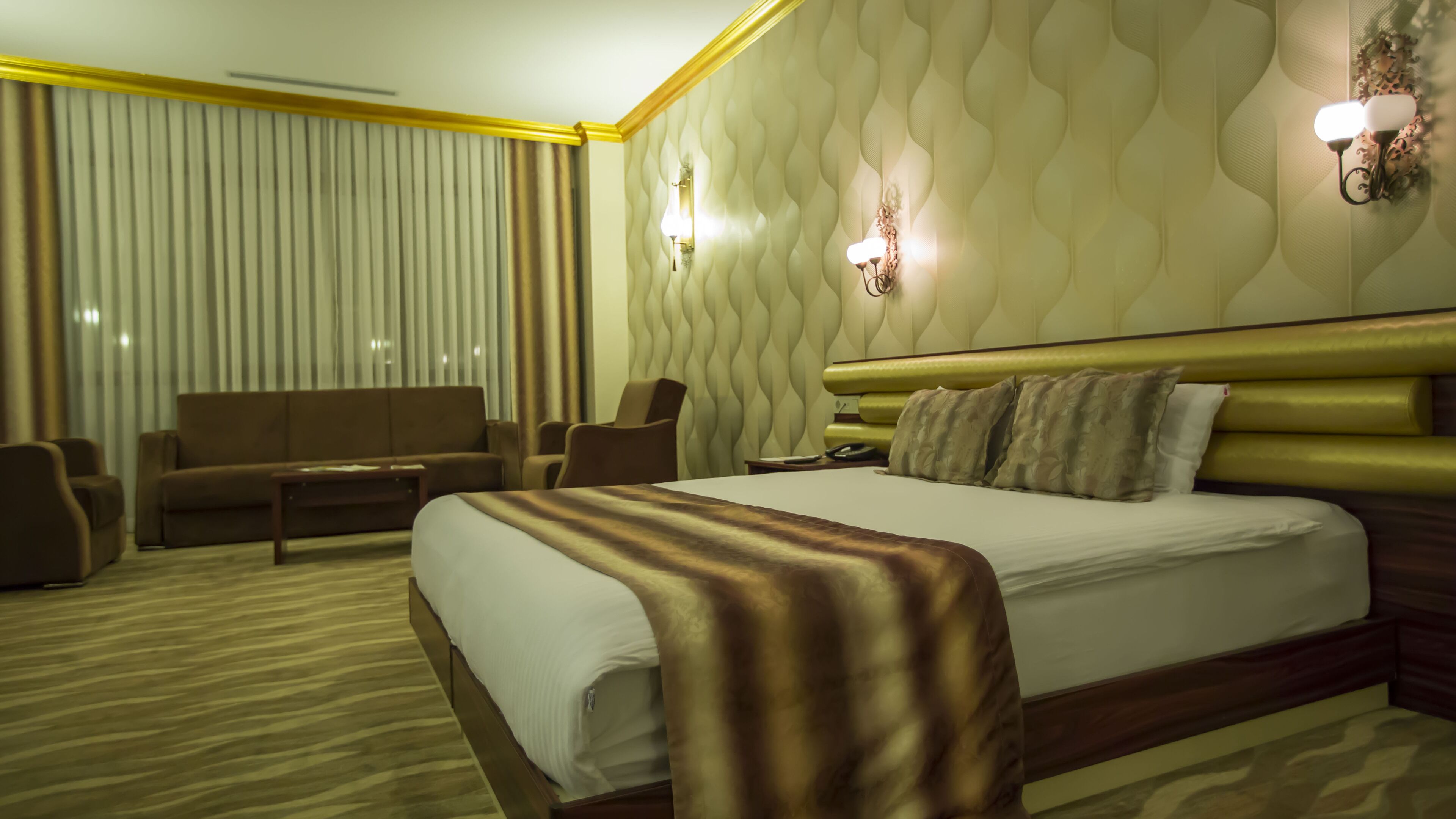 A hotel room with a large bed, a sofa, two armchairs, a bedside table, and a lamp.