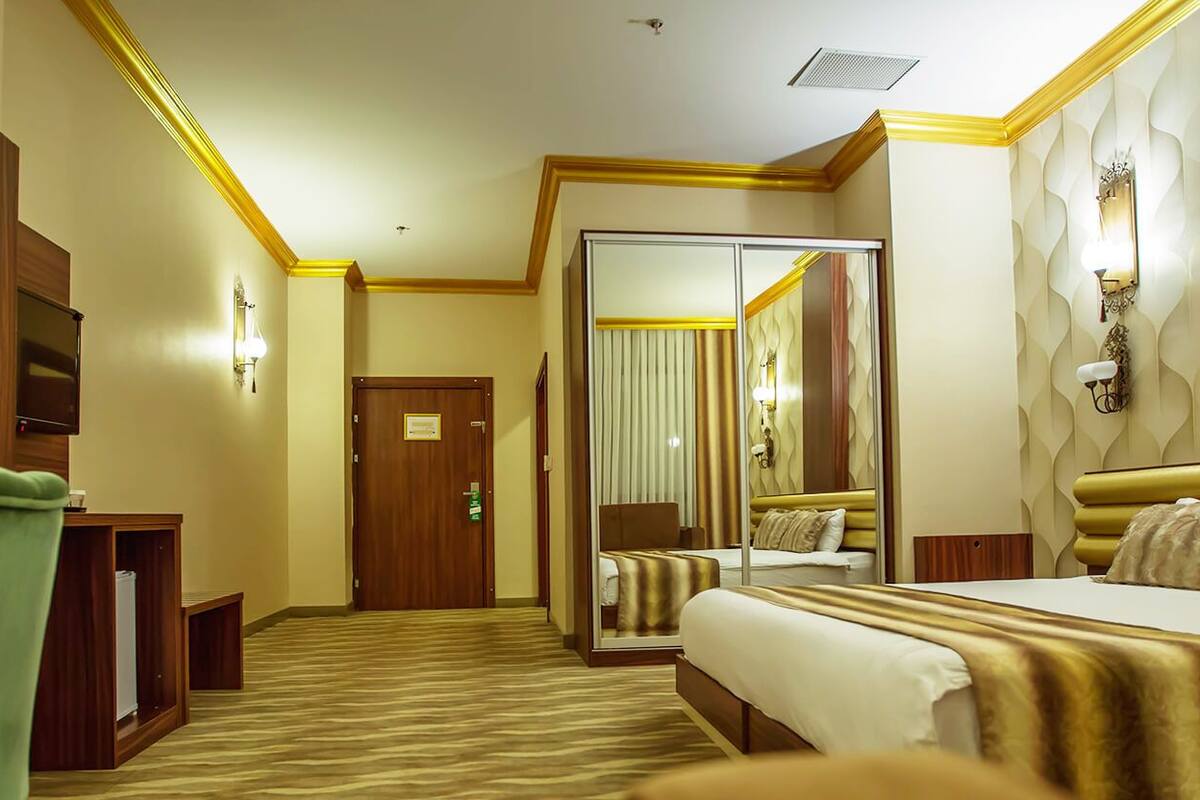 A hotel room with a bed, a desk, a chair, a mirror, and a door.