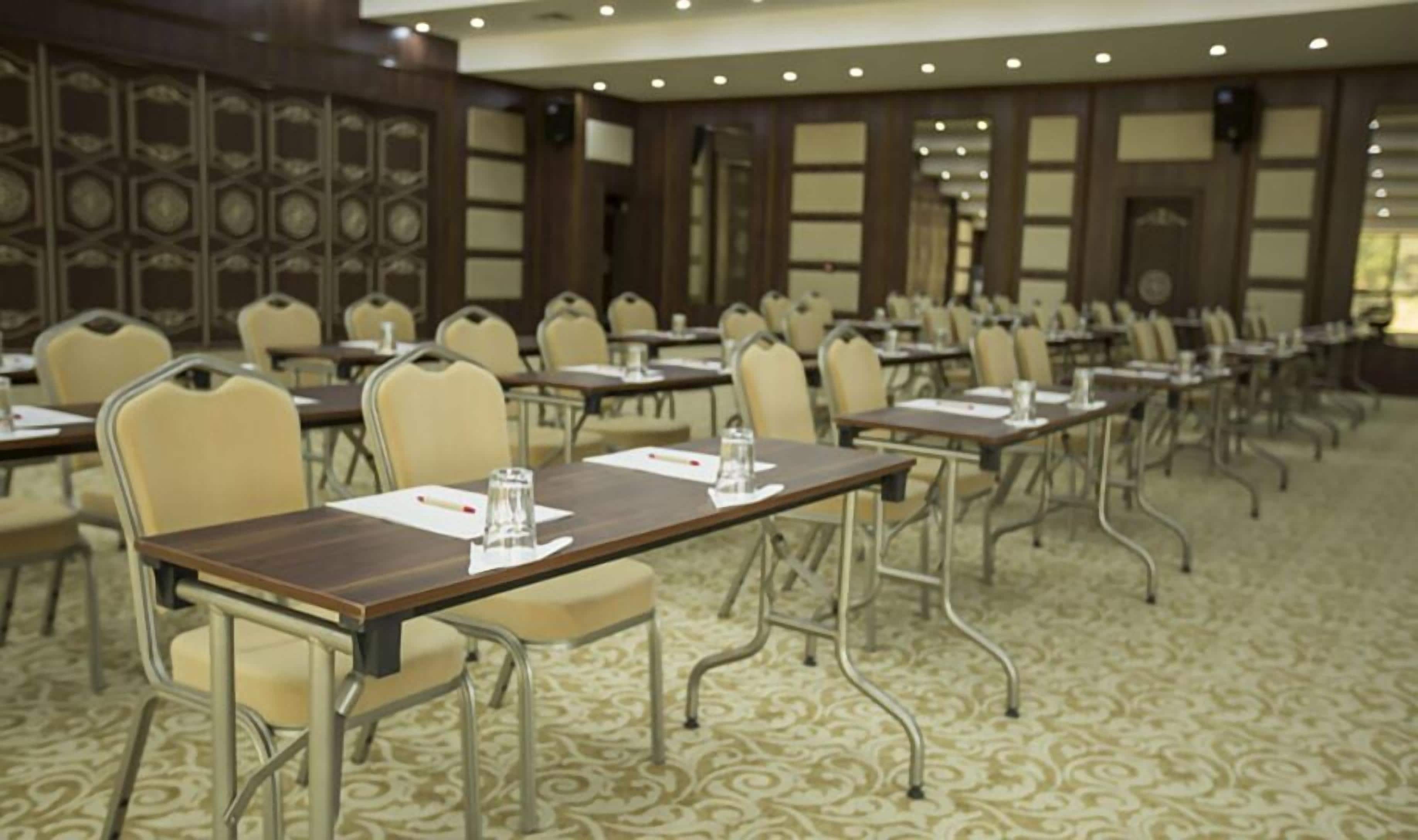 A conference room with rows of tables and chairs, equipped with water bottles and notepads.