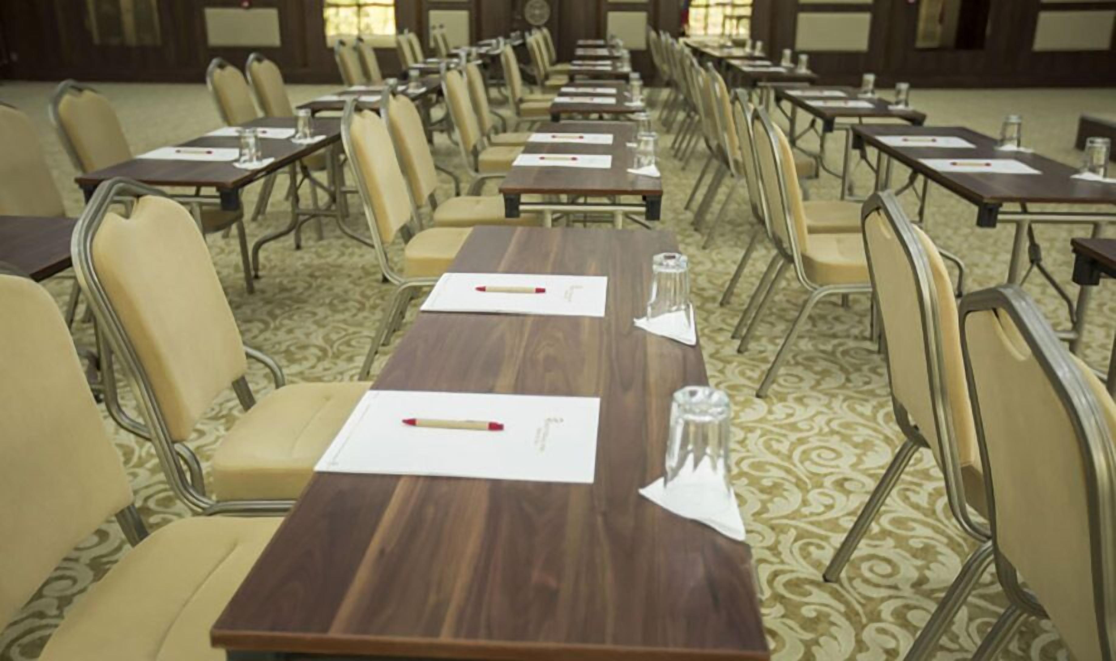 A conference room with rows of tables and chairs, equipped with nameplates and pens.
