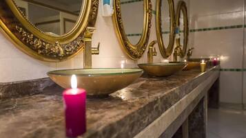 A bathroom with three gold-framed mirrors, a pink candle, and two glass bowls on a marble countertop.
