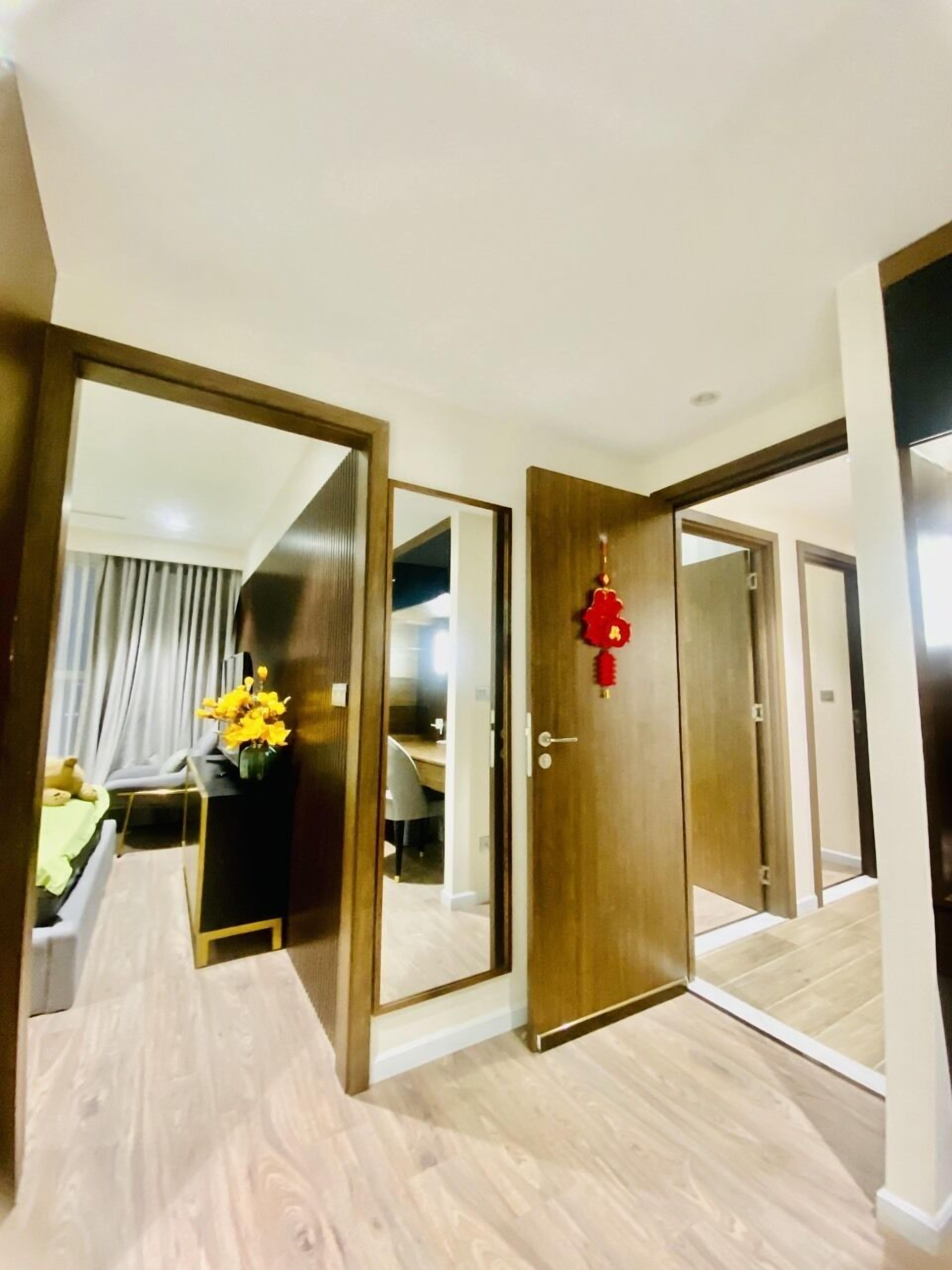 A hotel room with a wooden floor, a bed with a green bedspread, a desk with a chair, and a mirror reflecting the room.
