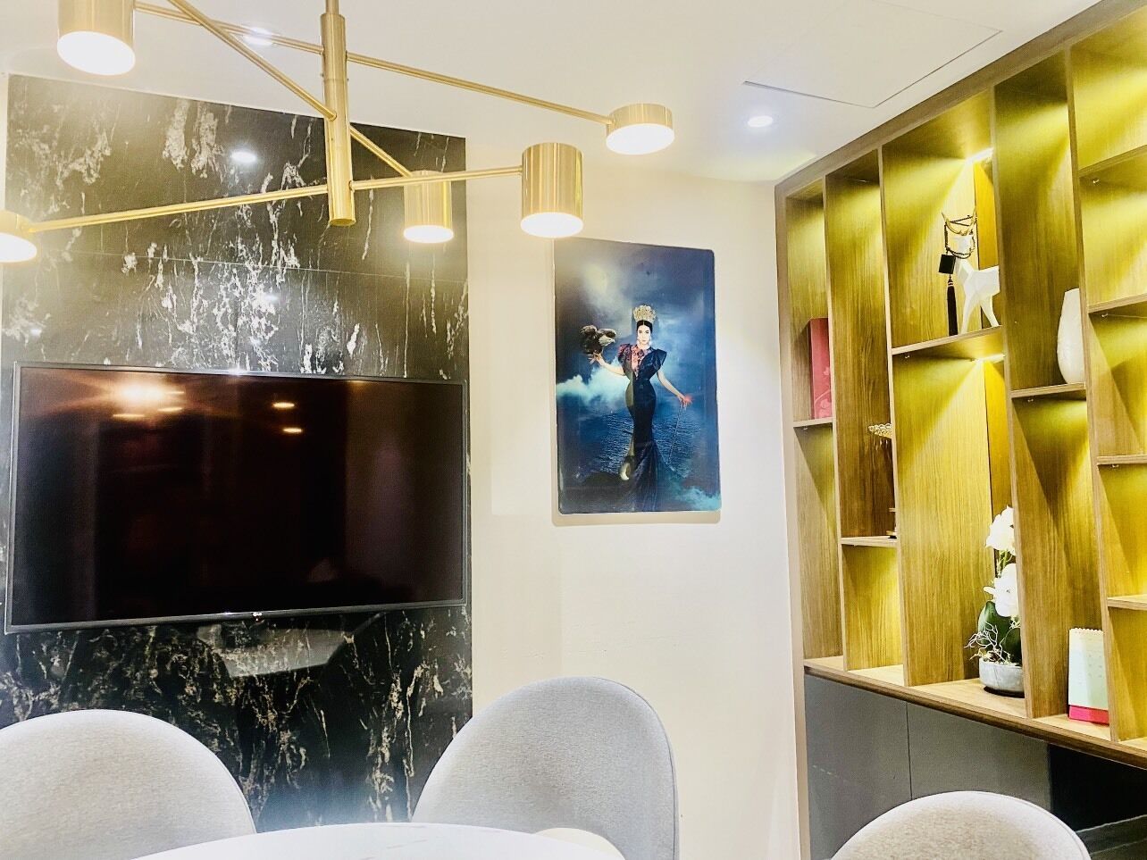 Una sala de estar moderna con un televisor de pantalla plana, una pared decorativa de mármol, una estantería dorada y una obra de arte enmarcada.