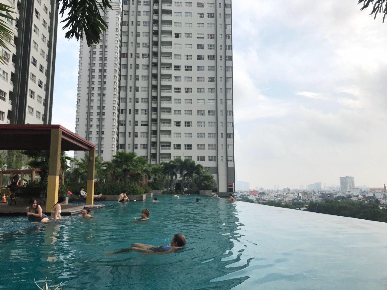 A swimming pool with people relaxing, surrounded by tall residential buildings and greenery.