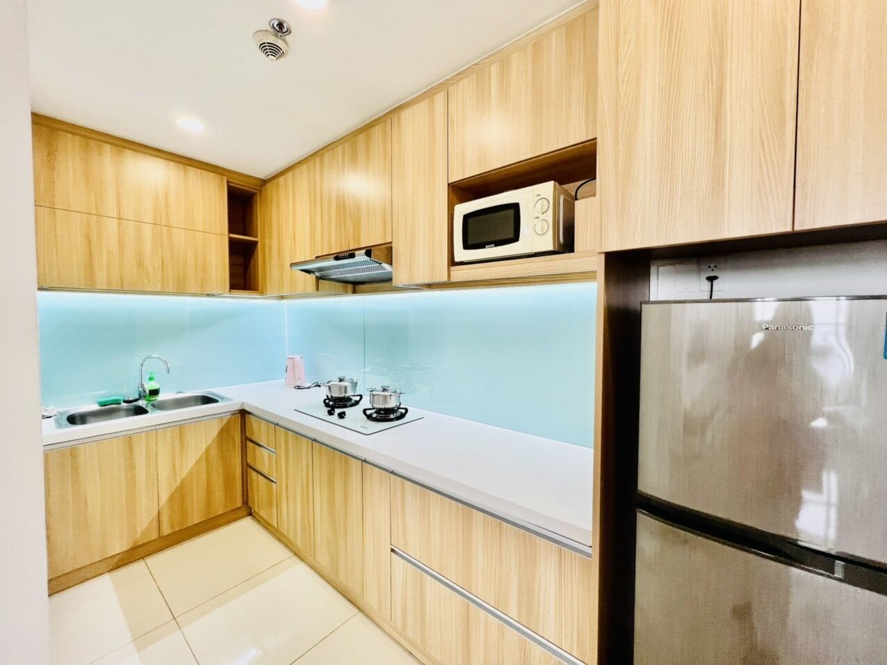 A modern kitchen with wooden cabinets, a stainless steel refrigerator, a microwave, and a gas stove.