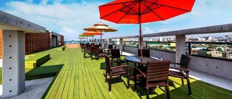 A rooftop terrace with outdoor seating, umbrellas, and a city view.