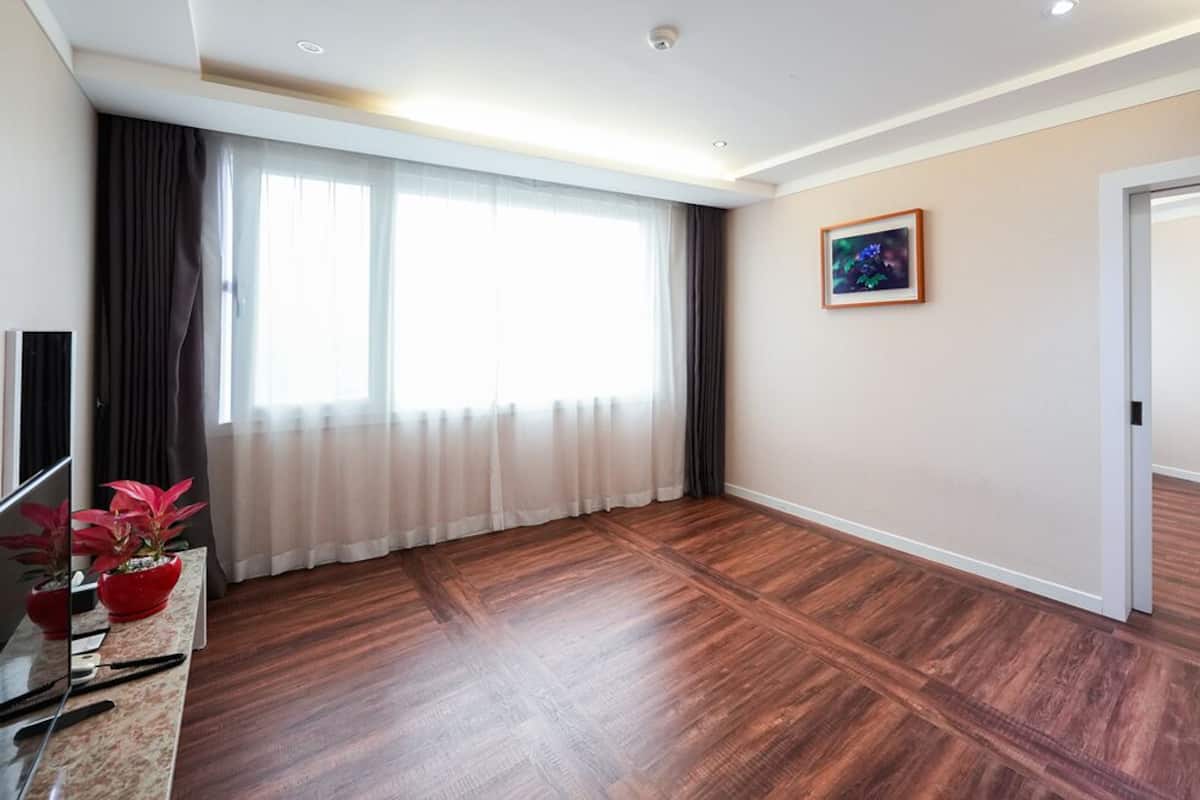 Une pièce spacieuse avec une grande fenêtre, un plancher en bois, une porte et un tableau encadré au mur.