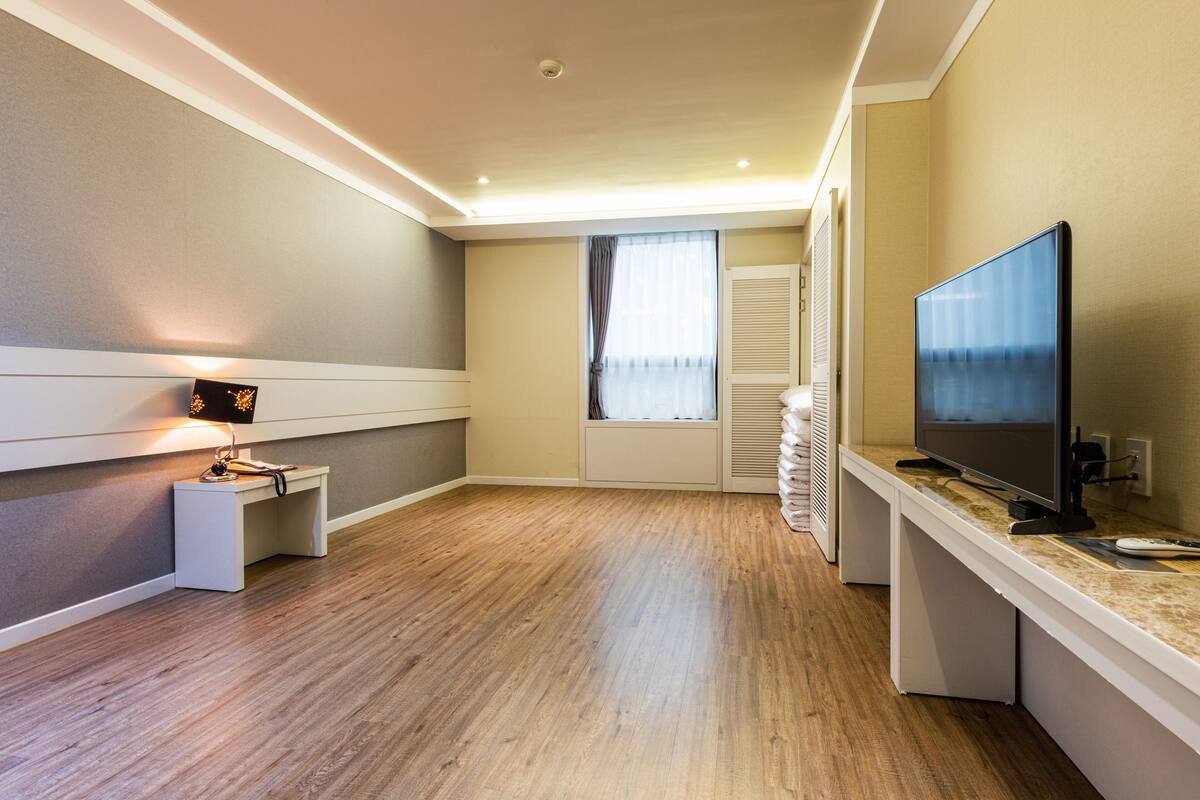 Une chambre d’hôtel moderne avec un plancher en bois, un téléviseur à écran plat, un petit bureau avec une lampe et une fenêtre avec des rideaux.